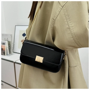 Detail of glossy black shoulder bag with gold chain strap and metal clasp on beige trench coat