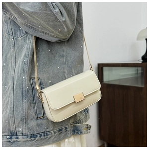 Close-up of minimalist cream-white leather crossbody bag with gold buckle and chain