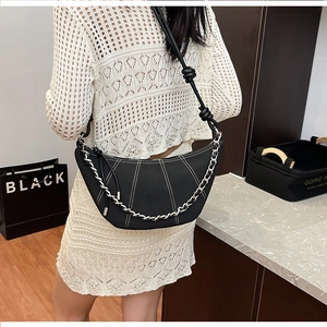 Detail of black leather crescent bag with white contrast stitching and silver chain strap