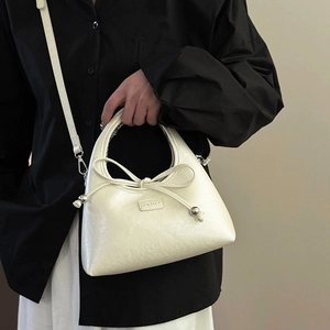 Minimalist cream white leather dumpling bag with bow detail worn as a crossbody shoulder bag
