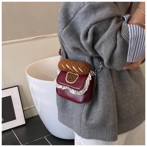 Detail view of mini burgundy crossbody bag with lace trim and plush bread charm