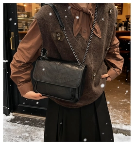 Detail of black chevron quilted leather bag with dark metal chain strap in winter setting