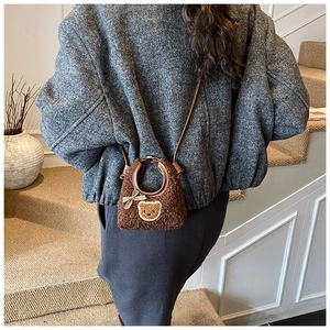 Détail d'un petit sac en peluche ours avec nœud porté à l'épaule par un enfant
