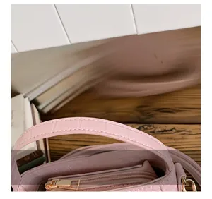 Close-up of pink handbag with crocodile texture, reinforced handle and gold metal zipper