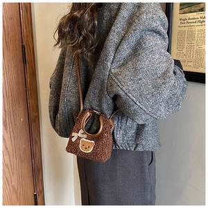 Détail d'un mini sac en peluche marron avec ours et nœud porté à l'épaule par un enfant