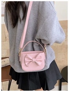 Detail of pink faux crocodile leather bag with large bow and golden metal hardware