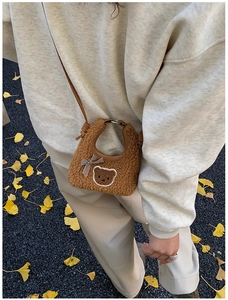 Détail du sac en peluche ours brun avec nœud à carreaux sur fond de feuilles d'automne