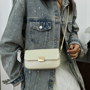 Minimalist beige crossbody bag with gold hardware and chain strap on denim jacket