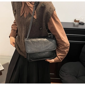 Detailed view of the V-quilted texture and silver chain strap on a black messenger bag