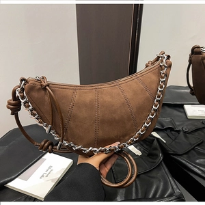 Detail of a brown suede croissant bag featuring silver chain and knotted strap accents