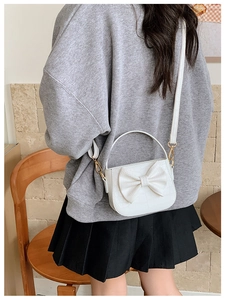 Detailed view of white crocodile pattern crossbody bag with a bow on girl outfit