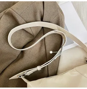 Detail of adjustable cream PU leather shoulder strap with metallic eyelets on crossbody bag