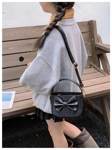 Detail of black girl's crossbody bag featuring crocodile pattern and large bow decoration