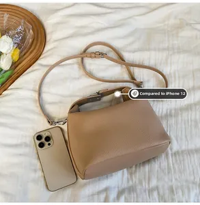 Größenvergleich der braunen Lederhandtasche mit einem iPhone auf weißem Stoffhintergrund