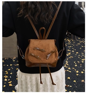 Close-up of a brown suede backpack with bow details and leather straps worn by a model