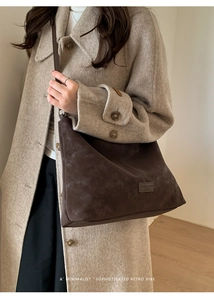 Detail of minimalist retro brown suede crossbody tote worn with a wool coat in a bright room