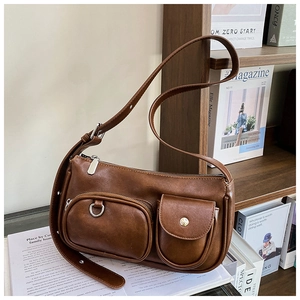 Detail of a brown leather bag with dual front utility pockets on a lifestyle shelf