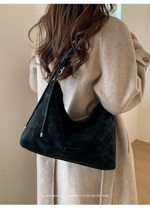 Detail of minimalist black suede hobo bag with a leather strap wrap and logo patch