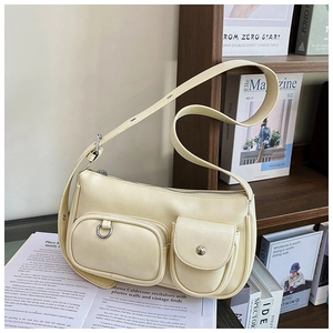 Detail of a chic cream underarm bag with functional outer pockets on a wooden shelf