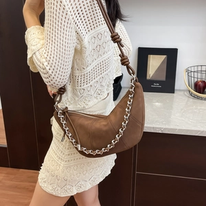 Sac hobo en daim marron avec détails matelassés et chaîne argentée porté sur robe blanche