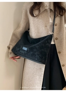 Detail shot of a black suede hobo bag with a minimalist logo patch on a beige coat