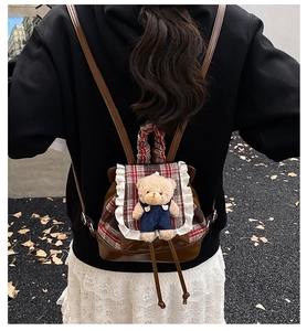 Rear view of a cute brown bear toddler backpack with red plaid lace trim and plush toy
