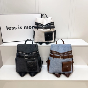 Three color-block canvas backpacks with leather flaps and buckle straps on white stand