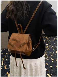Close-up of small brown leather backpack with bow details and autumn leaf background
