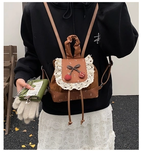 Détail d'un sac à dos floral vintage avec dentelle blanche et pompons cerises