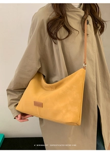 Detail of yellow matte leather half-moon tote bag with logo on a khaki trench coat