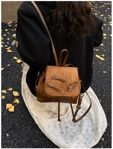 Close-up of brown suede backpack with bow details and drawstring closure on autumn road