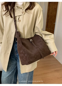 Détail du grand sac seau en daim marron avec boucle rétro porté sur un manteau beige