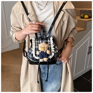Detail of toddler backpack featuring checkered pattern, lace trim, and plush bear doll
