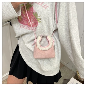 Detail of pink faux suede crossbody bag with white sherpa trim on model for styling