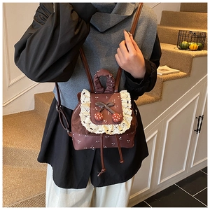 Détail d'un mini sac à dos marron avec bordure en dentelle, nœud et breloques fraises