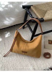 Detail of a ginger suede hobo bag with a knotted strap on a textured beige rug