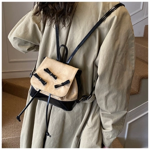 Detail of a mini backpack featuring beige suede flap with three black leather bows decoration