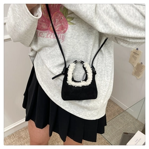 Detailed close-up of a black suede dumpling bag with soft white faux fur trim handles