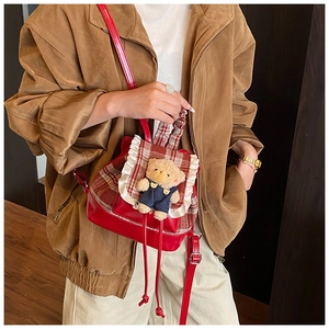 Detail of red checkered schoolbag featuring white lace trim and cute teddy bear pendant
