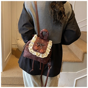 Détail d'un mini sac à dos marron vintage avec bordures en dentelle et cerises