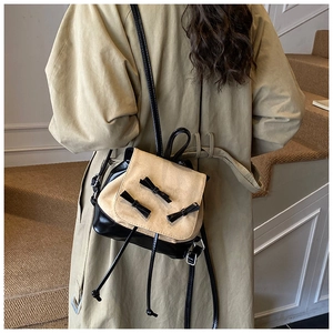 Detail of canvas mini backpack with black bows and drawstring on a model wearing a coat