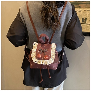 Détail d'un sac à dos vintage pour étudiant avec dentelle blanche et pendentif fraise