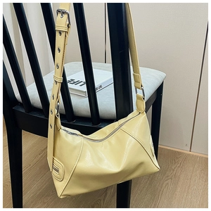 Detail of light yellow PU half-moon bag with wide metal eyelet strap on a chair