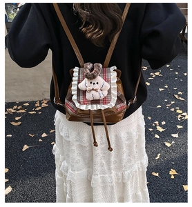 Detalle de mochila infantil a cuadros con ribete de encaje blanco y colgante de perro suave
