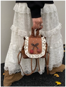 Détail du mini sac à dos en cuir caramel avec dentelle blanche et breloques cerise