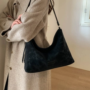 Minimalist black suede hobo shoulder bag shown on model in a stylish indoor setting