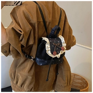 Détail d'un mini sac à dos noir avec bordure en dentelle blanche et charm fraise