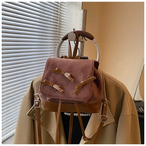 Detail of a brown and purple mini backpack featuring suede texture and leather bow accents