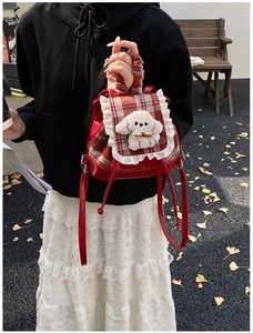 Detalle de mochila infantil a cuadros rojos con encaje y adorno de perro de peluche