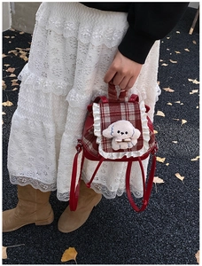 Detalle de mochila infantil de cuero rojo con solapa de cuadros, encaje y peluche de perro
